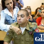 A man in military uniform sits on a wooden bench in a courtroom and is comforted by a woman.